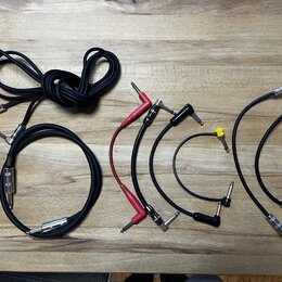 Sada různých audio kabelů s konektory typu jack položená na dřevěném stole. Je zde jeden dlouhý černý kabel, jeden kratší černý kabel s nápisem "KORD…