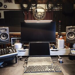 Fotografie zachycuje pracovní místo s hudební technikou. Jsou zde dva studiové monitory značky FOCAL, notebook, externí klávesnice a myš. V popředí j…