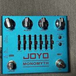 Modrý kytarový efekt s nápisy JOYO a MONOMYTH. Horní část obsahuje čtyři stříbrné otočné knoflíky s popisky VOICE, BLEND, LEVEL a DRIVE. Uprostřed je…