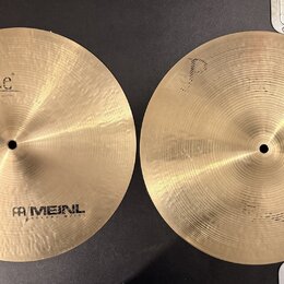 Dvě mosazné činely s jemným rýhováním povrchu. Levý činel nese nápisy „Byzance“ a „MEINL HOLANG MEINL“. Pravý činel nemá žádný viditelný nápis ani lo…