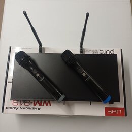 Dvě černé bezdrátové dynamické mikrofony s mřížkou leží na černém přijímači se dvěma anténami. Celý set je umístěn na bílém kartónovém obalu, na kter…