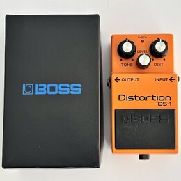 Oranžový kytarový efekt s černým spodním panelem a nápisy Distortion DS-1 a BOSS. Na horní části jsou tři černé otočné ovnovátka s popisky TONE, LEVE…