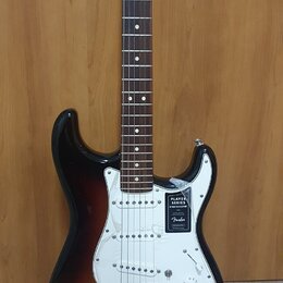 Elektrická kytara s tłem v barvě sunburst a bílým pickguardem. Na těle je nalepený štítek s nápisy PLAYER SERIES STRATOCASTER a logo Fender. Kytara m…