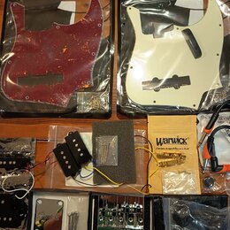 Sada příslušenství pro basovou kytaru rozložená na hnědém stole. V horní části jsou dvě pickguardy v plastových obalech značky FLEOR, jedna v červené…