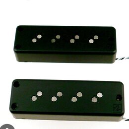 Dvě černé elektrické kytarové snímače typu humbucker s viditelnými kovovými póly. Spodní snímač má v pravém dolním rohu bílé logo ve tvaru stylizovan…