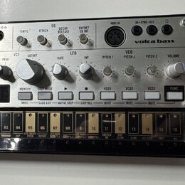 Stříbrný analogový syntetizátor s nápisy KORG a volca bass. Zařízení obsahuje řadu otočných knoflíků, tlačítek a digitální displej. V dolní části je…