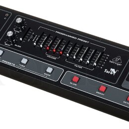 Černý syntetizátor s dřevěnými bočními panely. Na horním panelu jsou knoflíky, posuvníky a tlačítka s nápisy jako VOLUME, TUNE, BEAT, GLIDE a FILTER.…