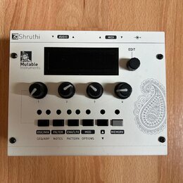Bílý elektronický modul s nápisem Shruthi a logem Mutable Instruments. Zařízení má čtyři černé otočné ovladače označené čísly 1 až 4, pět malých zele…