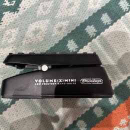 Černý volume pedál s nápisem VOLUME(X)MINI a LOW FRICTION BAND-DRIVE. Na pravé straně je umístěno logo Dunlop v oválu. Povrch pedálu vykazuje mírné z…