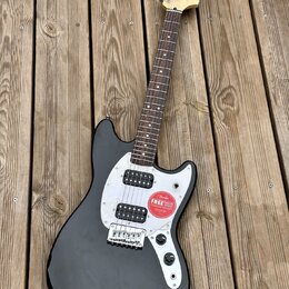 Černá elektrická kytara s bílým pickguardem a hnědým hmatníkem. Na hlavě je viditelné logo Squier. Kytara má dva snímače a na těle je nalepená červen…