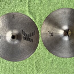 Dvě kovové činely v tmavém, matném provedení položené na zeleném textilu. Na obou je viditelné velké logo K a nápis LIGHT HIHAT BOTTOM 14"/35 cm. Pov…