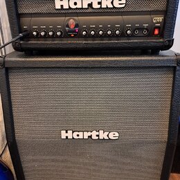 Kytarové kombo typu stack značky Hartke. Horní část tvoří zesilovač s ovládacími prvky, kde jsou viditelné nápisy INPUT, CRUNCH, VOLUME, BASS, TREBLE…