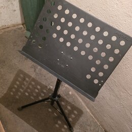Černý kovový notový stojan s perforovanou deskou. V pravém horním rohu desky je bílý nápis PROEL. Stojan stojí na trojnožce, povrch desky vykazuje dr…