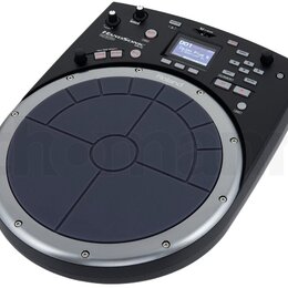 Elektronický perkusní pad černé barvy s modrým gumovým playing polem rozděleným na zóny. Na přístroji jsou viditelné nápisy HANDSONIC, HP-20 a Roland…