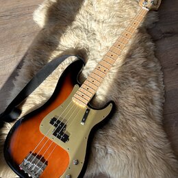 Elektrická basová kytara s tělem v provedení sunburst a zlatým pickguardem. Na hlavě hředu je viditelné logo Squier. Nástroj má světlou dřevěnou hmat…