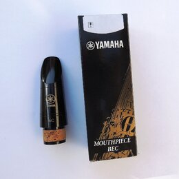Černý munzpun s korkem v dolní části a přiloženým černým papírovým krabicí. Na munzpunu i na krabici je bílé logo a nápis YAMAHA, na munzpunu je dále…