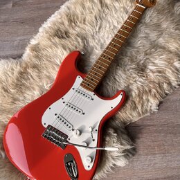 červená elektrická kytara s bílým pickguardem a hnědým hmatníkem. Na hlavě nástroje je viditelné logo Squier. Kytara má tři snímače, pětipositionní p…