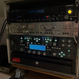 Stojan s rackovým vybavením v hliníkovém kufru na kolečkách. Jsou zde zařízení s nápisy SAMSON, PowerBrite PB11, M-AUDIO a PROFILER. Střední zařízení…