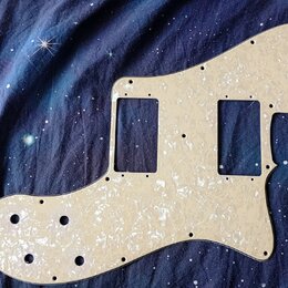 Bílá pickguard s perleťovým efektem pro elektrickou kytaru. Má dva obdélníkové výřezy pro snímače a několik kulatých otvorů na šrouby a ovládací prvk…