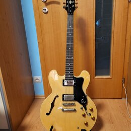 Světle žlutá polodublová elektrická kytara s černým hmatníkem a černým pickguardem. Na hlavě je bílý nápis Epiphone. Kytara má dva humbuckery, čtyři…