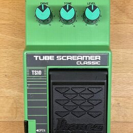 Zelený kytarový efekt s nápisy TUBE SCREAMER CLASSIC a TS10. Na horní části jsou tři modré otočné ovladače s popisky DRIVE, TONE a LEVEL. V dolní čás…