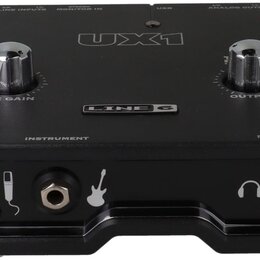 Černý zvukový interface s nápisy UX1 a LINE 6. Na horní straně jsou dva kovové otočné ovladače s popisky MIC GAIN a OUTPUT. V dolní části jsou vstupy…