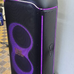 Černý party reproduktor s fialovým LED podsvícením. Na přední mřížce je umístěno zlaté logo JBL. Povrch je kombinací tkaniny a plastu s žebrovaným vz…