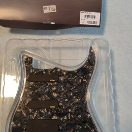 Sada předmontovaného pickguardu s mechanismy snímačů v průhledném plastovém obalu. Pickguard má černý mramorovaný vzor a tři černé snímače s bílým lo…