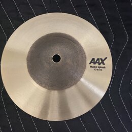 Kruhová činely typu splash v kovovém provedení s broušeným povrchem. Na pravé straně je černý nápis AAX a pod ním text MAXX Splash 7"/18 cm. Střed či…