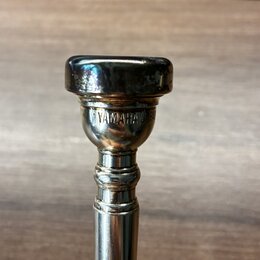 Detail horní části stříbrného kovového nástroje. Na povrchu je vyryt nápis YAMAHA JAPAN. Povrch vykazuje drobné škrábance a známky opotřebení.