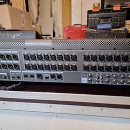Šedý rackový stagebox s řadou vstupních konektorů. Na horní části je viditelné logo behringer a v pravé části jsou vstupy označené od IN 1 do IN 24.…