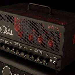 Černý kytarový zesilovač s kovovou mřížkou a rukojetí na horní straně. Na přední straně je bílý nápis Paul Reed Smith a červený nápis MT15. Spodní pa…