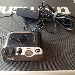 Kompaktní kytarový zesilovač černé barvy s kovovou rukojetí a stříbrným předním panelem. Na přístroji jsou nápisy Nutube, MV50 a VOX, dále označení V…