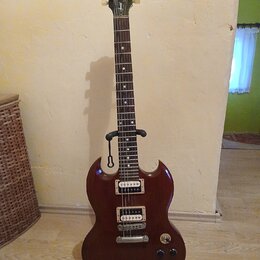 Tmavě hnědá elektrická kytara s dvojstupňovými humbuckery, umístěná na černém stojanu. Na hlavě nástroje je bílý nápis Gibson a pod ním v kurzivě Epi…