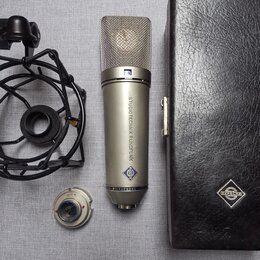 Stříbrný kondenzátorový mikrofon s kovovou síťovkou a nápisem STUDIOTECHNIK RUNDFUNK a MICROPHONE. Na těle je viditelné modré logo ve tvaru kosočtver…