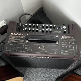 Hnědý akustický zesilovač s nápisem MOOGER a označením modelu SDSØA ACOUSTIC AMPLIFIER. Horní panel obsahuje ovládací knoflíky, přepínače a vstupy, z…