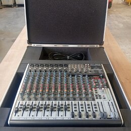 Míchací pult v ochranném přepravním kufru s černým polstrováním. Na horním pravém rohu je viditelné logo "Behringer". Zařízení obsahuje řadu faderů,…