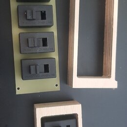 Na fotografii jsou čtyři černé elektrické spínače. Tři z nich jsou rozmístěny na zeleném obdélníkovém podkladu a jeden je umístěn v dřevěném rámečku.…