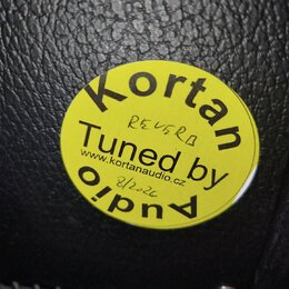 Kruhová žlutá nálepka s černým textem nalepená na černém povrchu z imitace kůže. Na nálepce je nápis Kortan Tuned by Audio a webová adresa www.kortan…