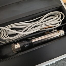 V černé přepravce s polstrováním se nachází mikrofon a bílý kabel. Mikrofon má stříbrný kovový trup, černou horní část s mřížkou a v dolní části je v…