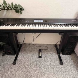 Černý digitální klavír s bílými a černými klávesami, umístěný na černém stojanu. Na pravé straně horního panelu je nápis NANTILUS. Instrument je dopl…
