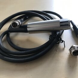 Na fotografii je černý kabel s kovovým cylindrickým koncem, který má v horní části svislé rýhy. Na kabelu je viditelný bílý nápis SHURE. Součástí jso…