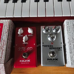 Čtyři kytarové efekty značky NUX z řady Reissue Series. Dva červené pedály mají nápis XTC OD, jeden stříbrný pedal má nápis STEEL SINGER DRIVE a posl…