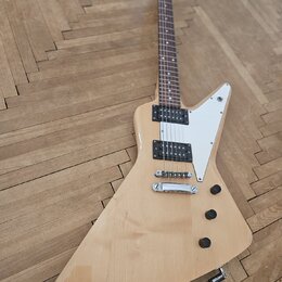Elektrická kytara s přírodním dřevěným povrchem a bílým plechtrátem. Nástroj má dva humbuckery, jeden tónový potenciometr a jeden přepínač. Na hředel…