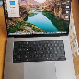 Stříbrný notebook MacBook Pro s otevřeným displejem. Na obrazovce je vidět okno „O tomto Macu“ s nápisem MacBook Pro a v pozadí krajinná fotografie.…