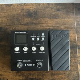 Černý kytarový procesor NUX MG-300 s připojeným expresním pedálem. Na zařízení jsou viditelné nápisy MG-300 MODELLING GUITAR PROCESSOR, EDIT/EXIT, SA…