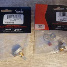 Dvě balená příslušenství značky Fender v plastových sáčcích s červeným a černým kartonem. Na obou je uveden nápis Genuine Fender parts, P.N. 09908340…