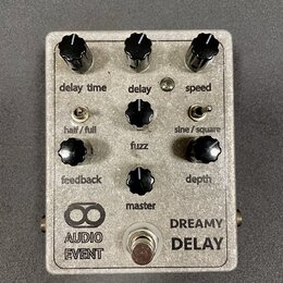 Stříbrný efektový pedál s nápisy AUDIO EVENT a DREAMY DELAY. Zařízení má šest černých otočných knoflíků s popisky delay time, delay, speed, feedback,…
