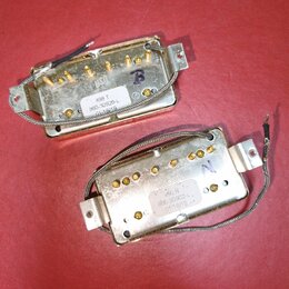 Dvě elektrické kytarové snímače v zlatavém kovovém provedení. Na horním je nálepka s nápisem 498 T, 860-30926-L a datem 01/18/19. Spodní snímač má na…