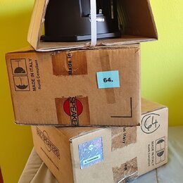 Tři hnědé kartonové krabice naskládané na sebe, z horní vykukuje černý reproduktorový magnet. Na krabicích jsou vidět nápisy MADE IN ITALY, RoHS Comp…